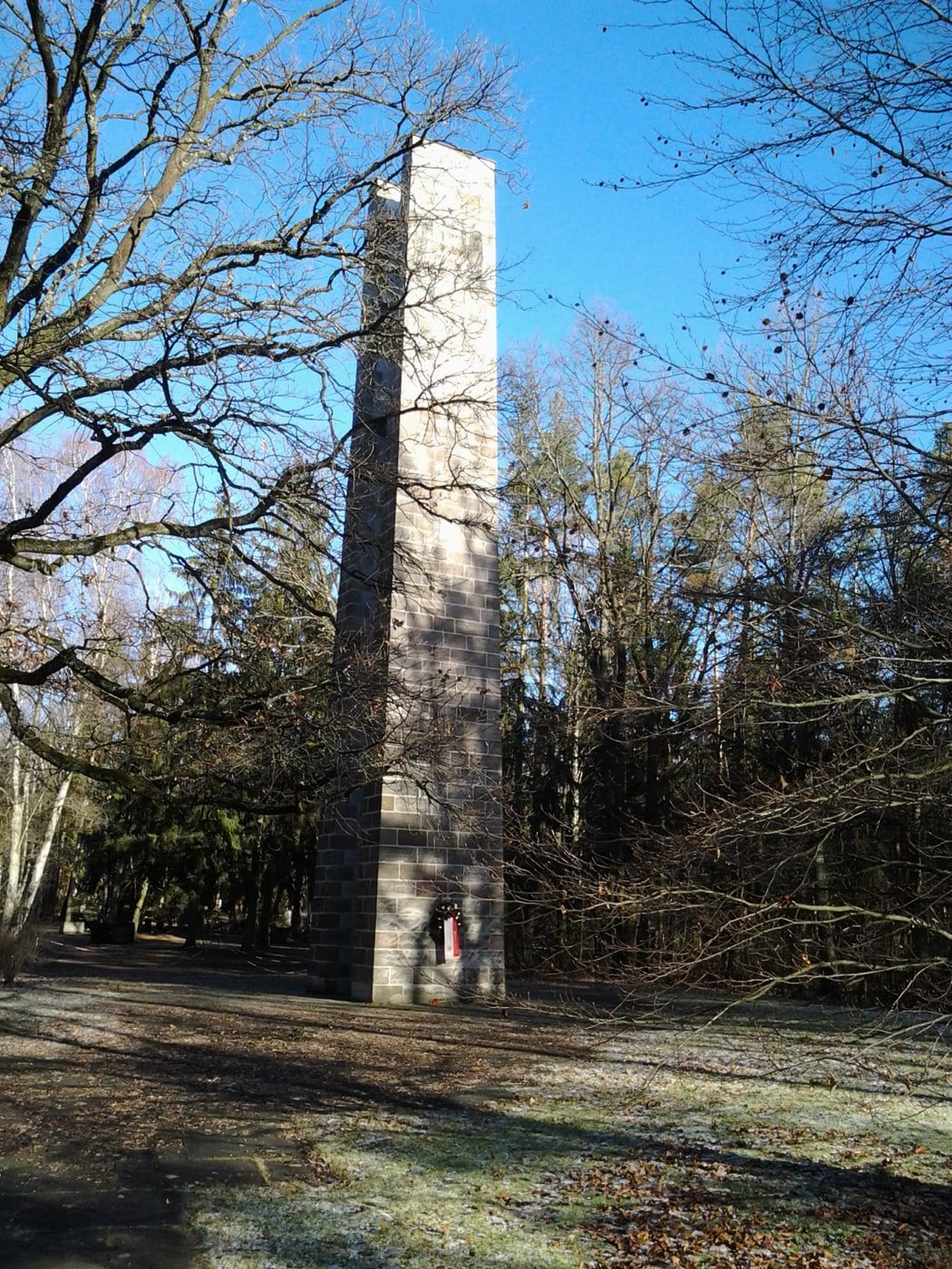 Hoher rechteckiger Glockenturm zwischen kahlen Bäumen auf bereiftem Boden auf Südfriedhof Nürnberg